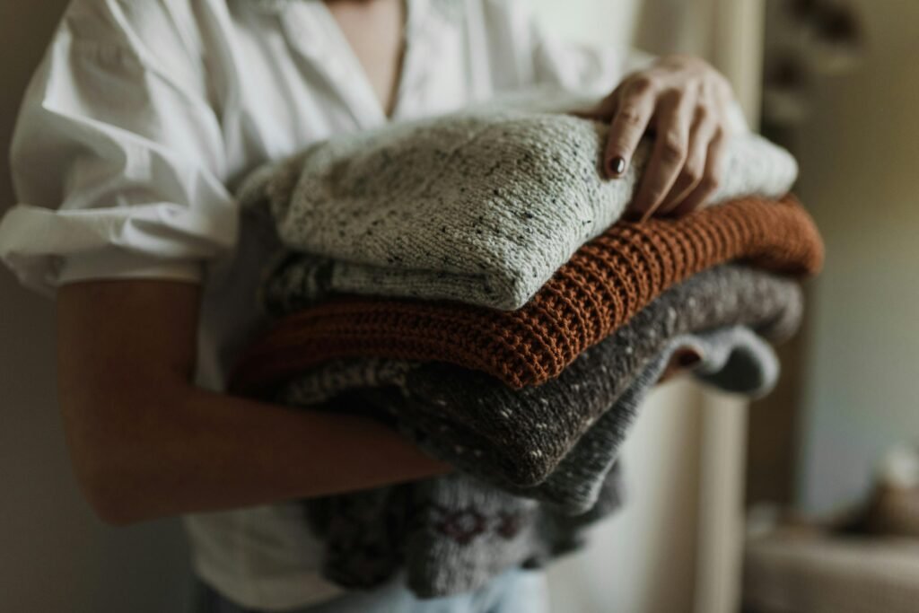 A woman holding folded winter sweaters in different colors