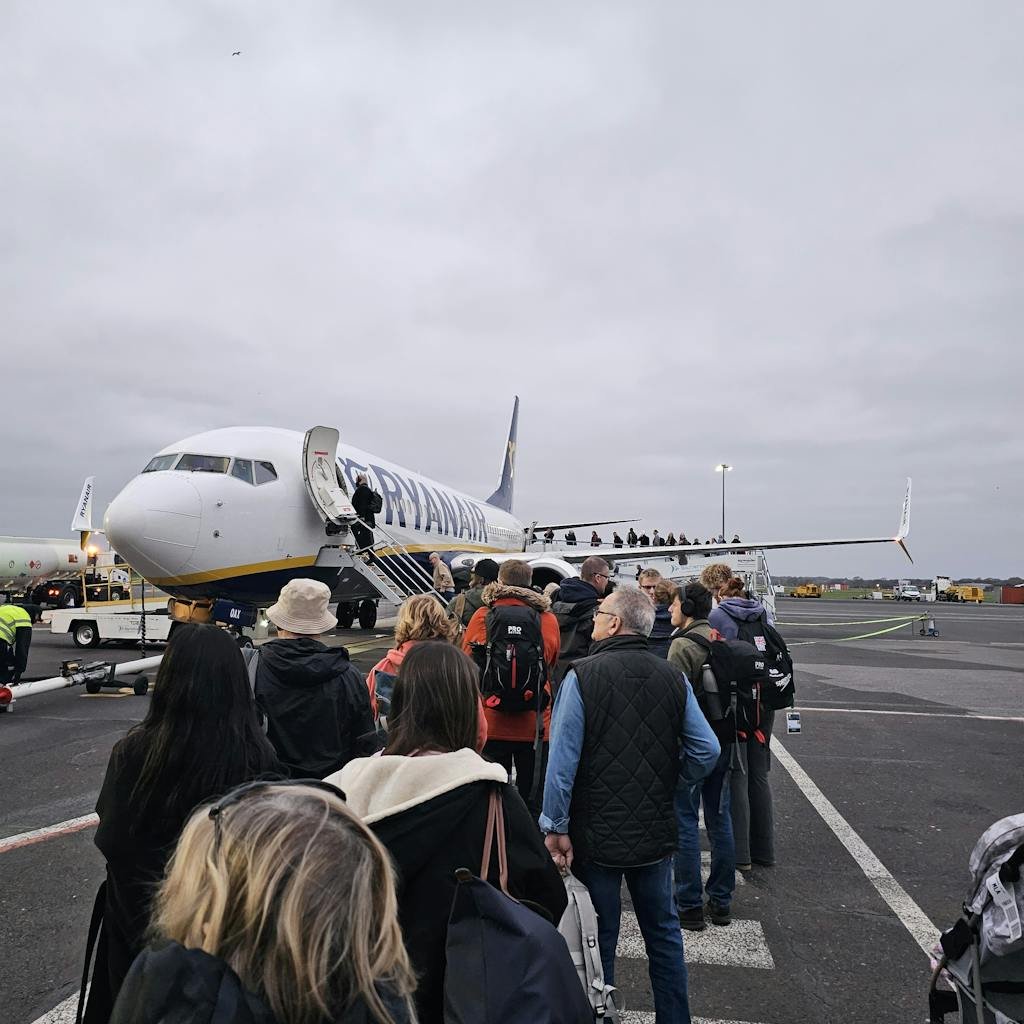 Travelers queue to board a Ryanair aircraft on an overcast day, capturing a common travel scene.
