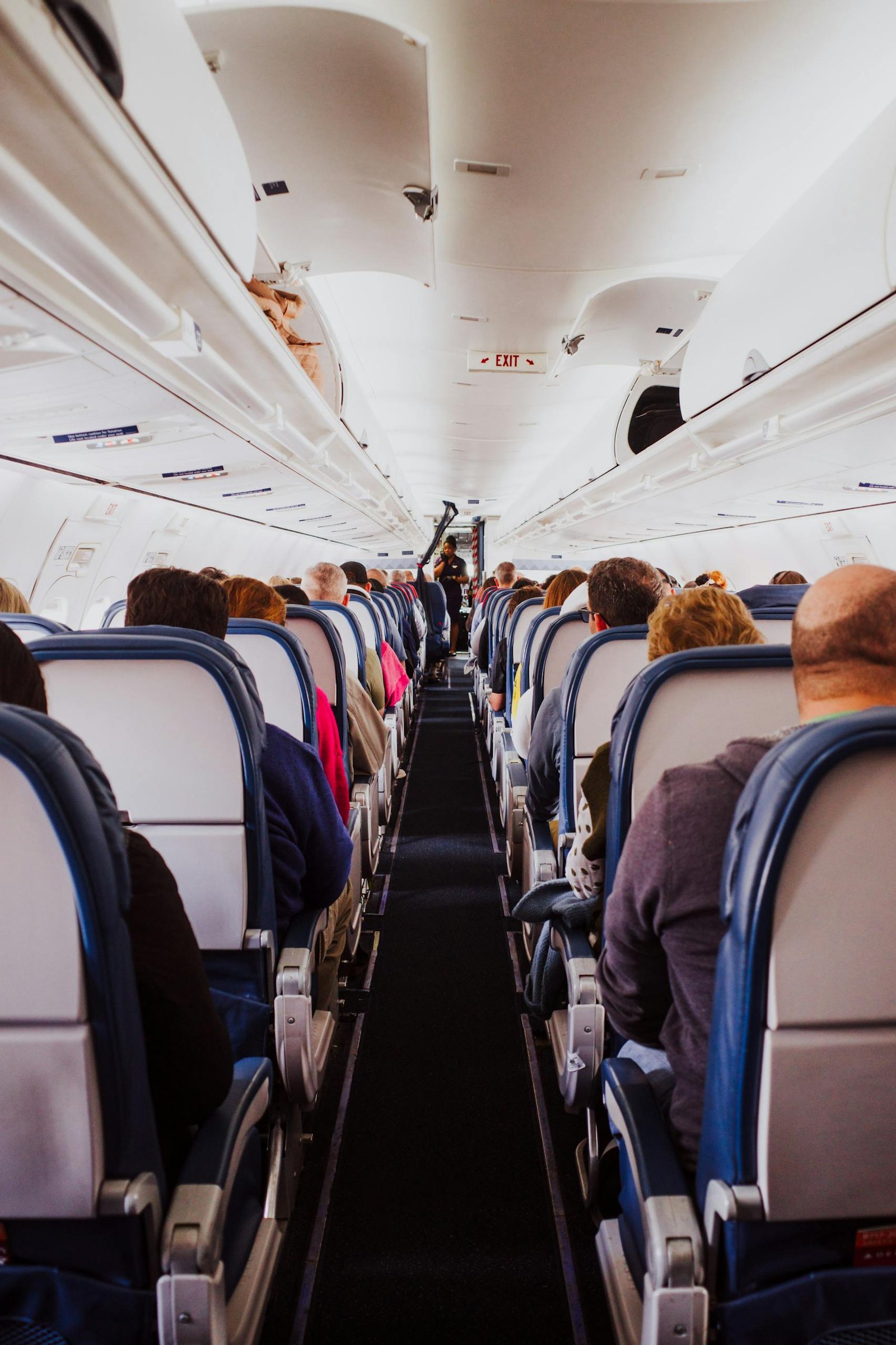 View from the back of a crowded airplane cabin showing passengers seated in rows during flight.