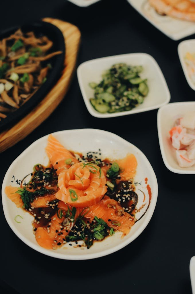 A beautifully arranged sushi platter featuring fresh salmon sashimi garnished with greens and sesame seeds.