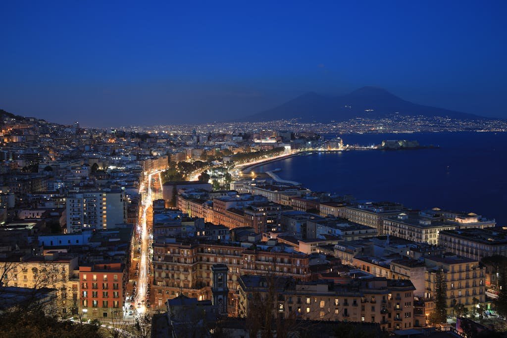 Is Naples Worth Visiting? 15 Pros and 5 Cons 5 A breathtaking aerial view of Naples cityscape and Mount Vesuvius under evening lights.