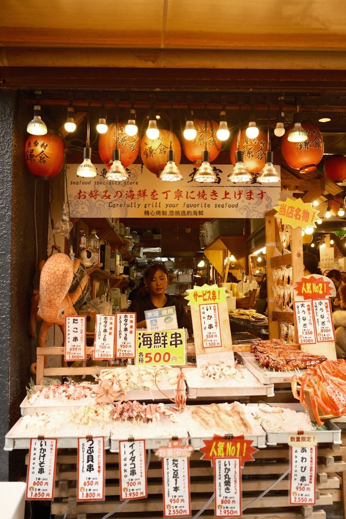 14 Best Things to Do in Kyoto, Japan + Travel Tips (2026) 12 A colorful seafood stall with lanterns at a bustling Japanese market displaying fresh seafood.