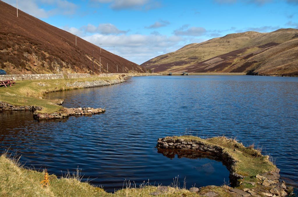 A serene mountain lake reflecting clear blue skies with lush green hills in the background.