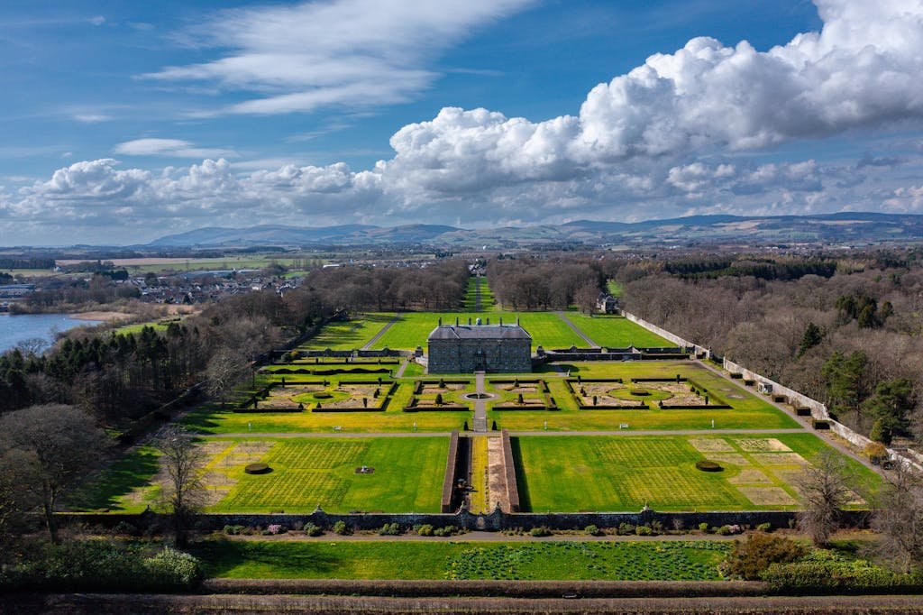 A stunning aerial view of a historic Scottish manor surrounded by lush gardens and green lawns.