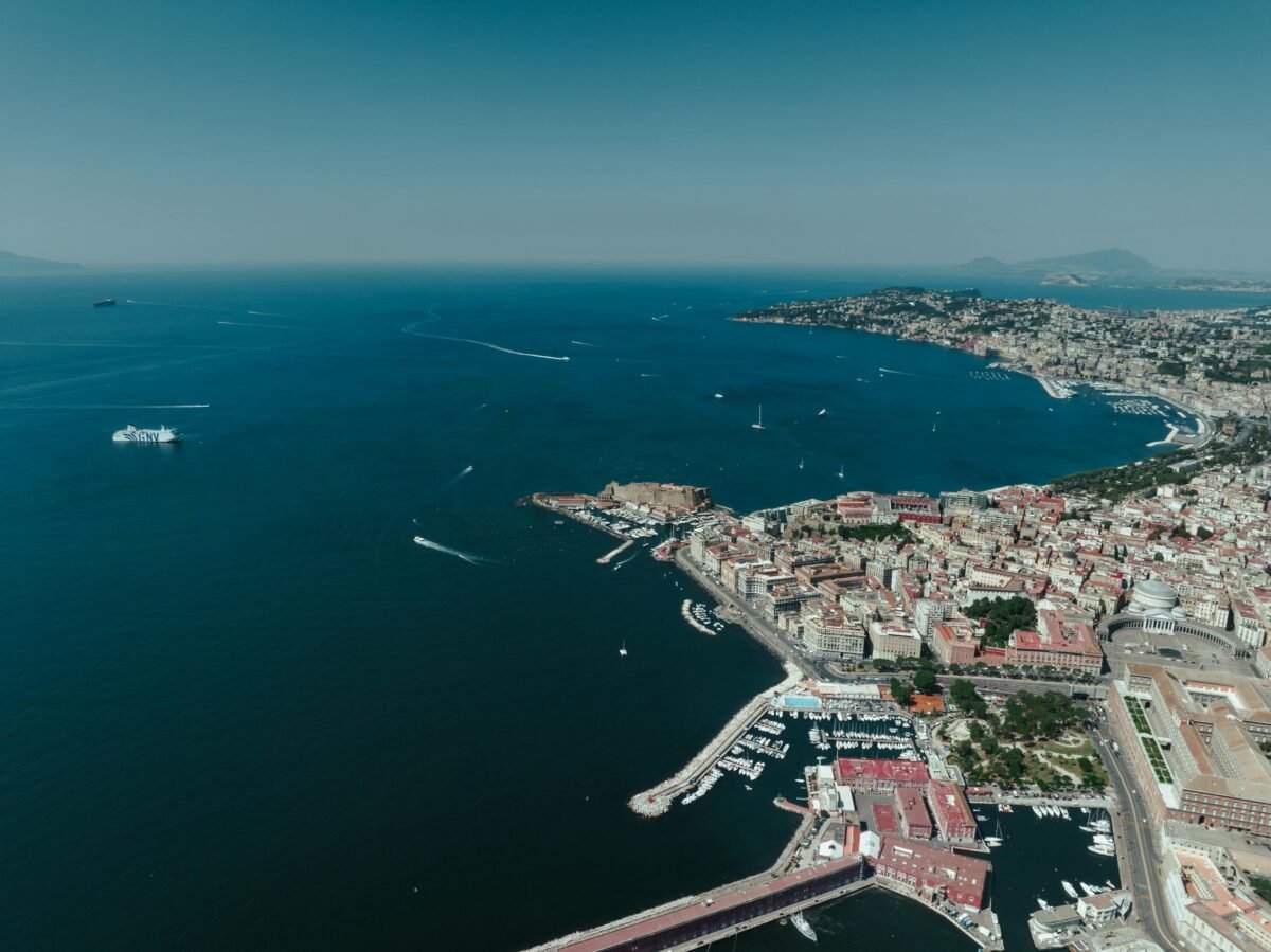 A stunning aerial view showcasing the vibrant city of Napoli, its bustling harbor, and the scenic Mediterranean coastline.