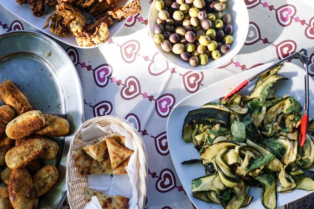 A vibrant top view photo of Mediterranean dishes including olives, zucchini, and various fried delicacies on a decorative tablecloth.