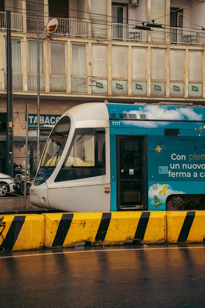 A vibrant tram passing through a rainy urban street in Naples, Italy, showcasing local architecture.