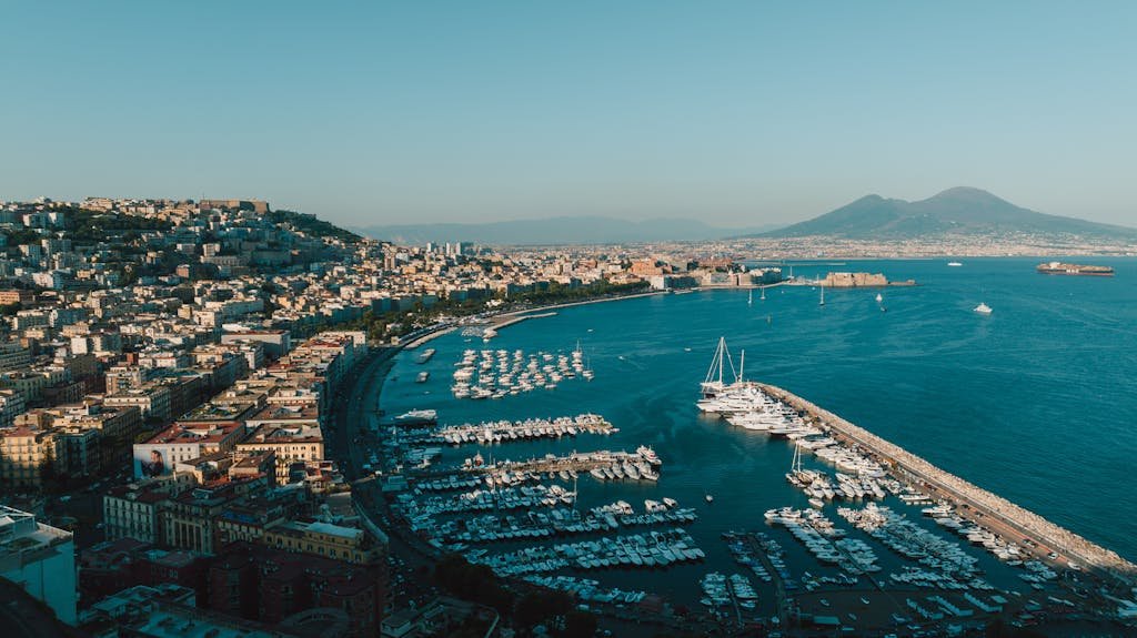 Aerial view of Naples harbor with boats and city skyline under clear blue sky.