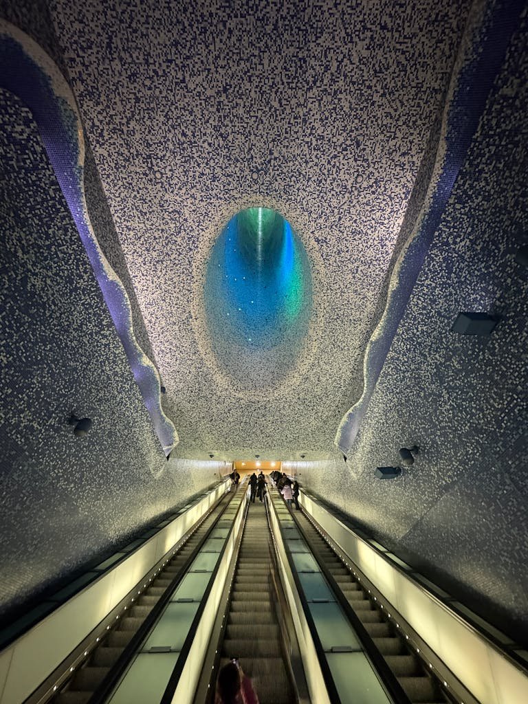 Artistic ceiling design of metro station in Naples, Italy, with people on escalator.