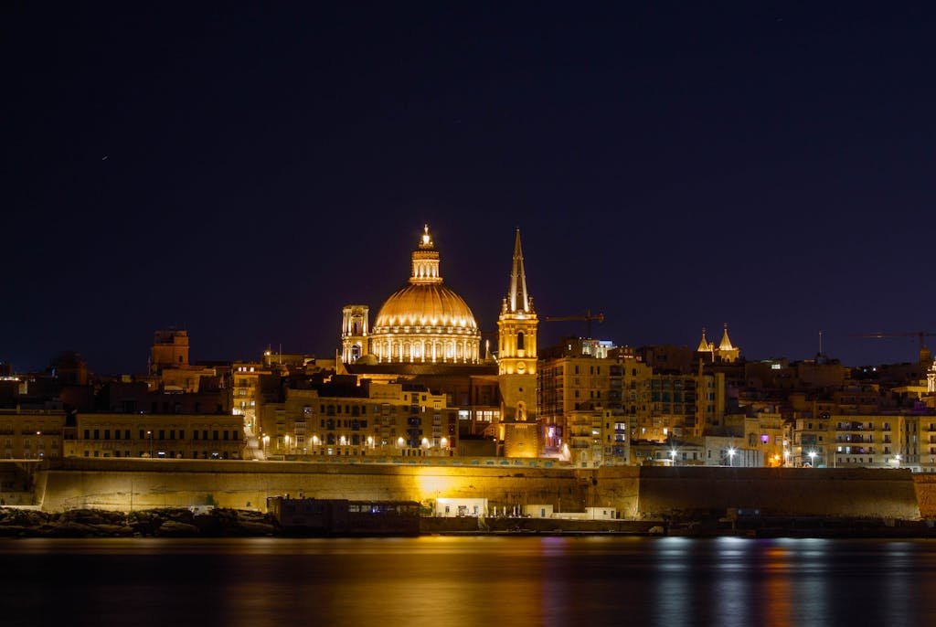 Beautiful night view of Valletta's illuminated skyline, showcasing iconic landmarks under a clear sky.