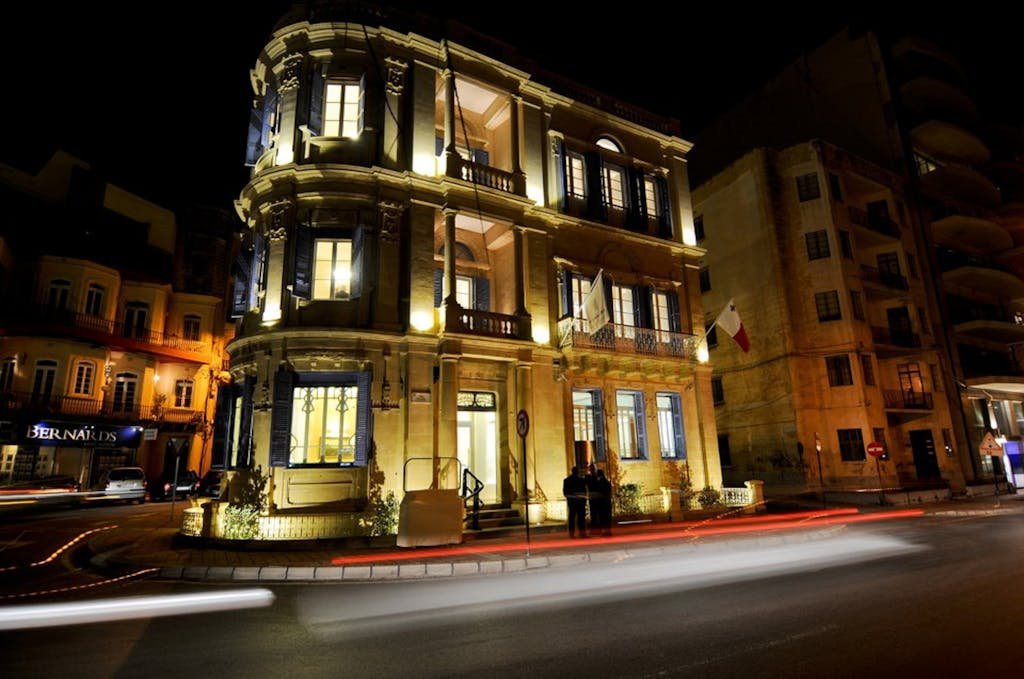 Beautifully lit historic building on a street corner in Sliema, Malta at night.