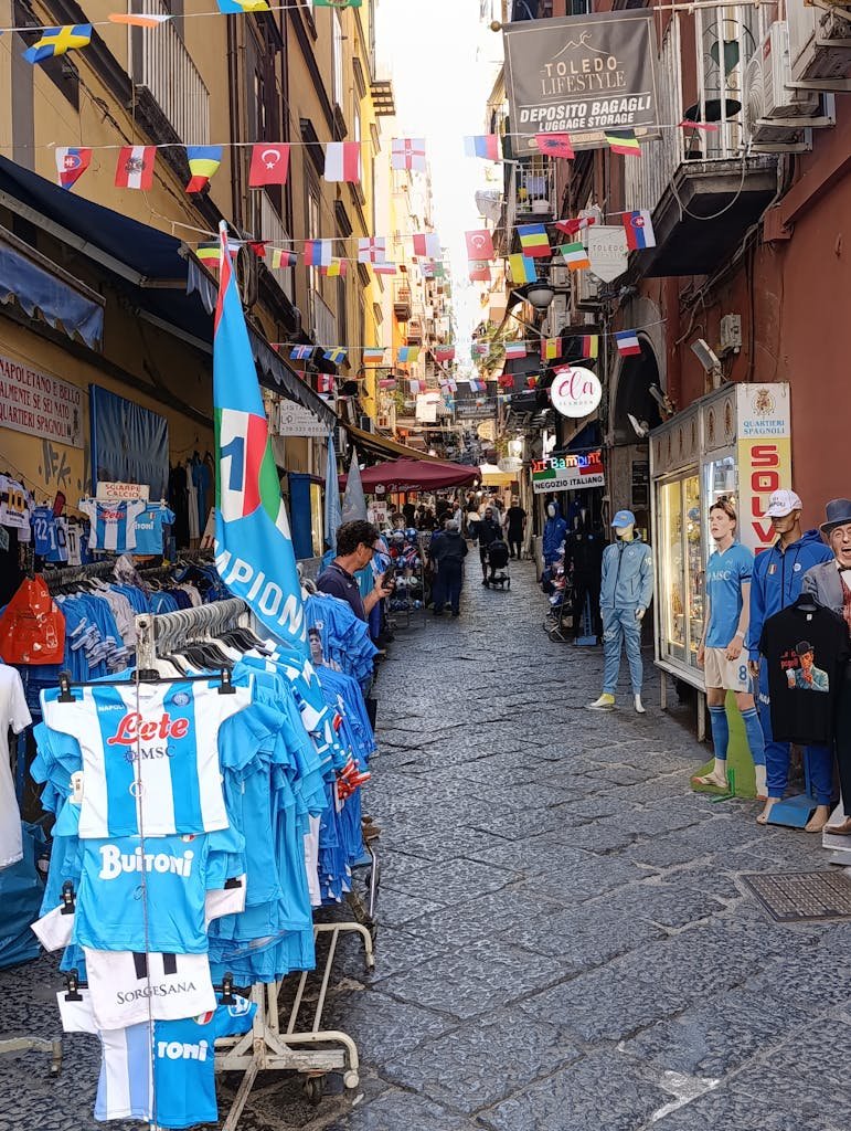 Is Naples Worth Visiting? 15 Pros and 5 Cons 11 Charming narrow alleyway in Naples with vibrant street market and blue football merchandise.