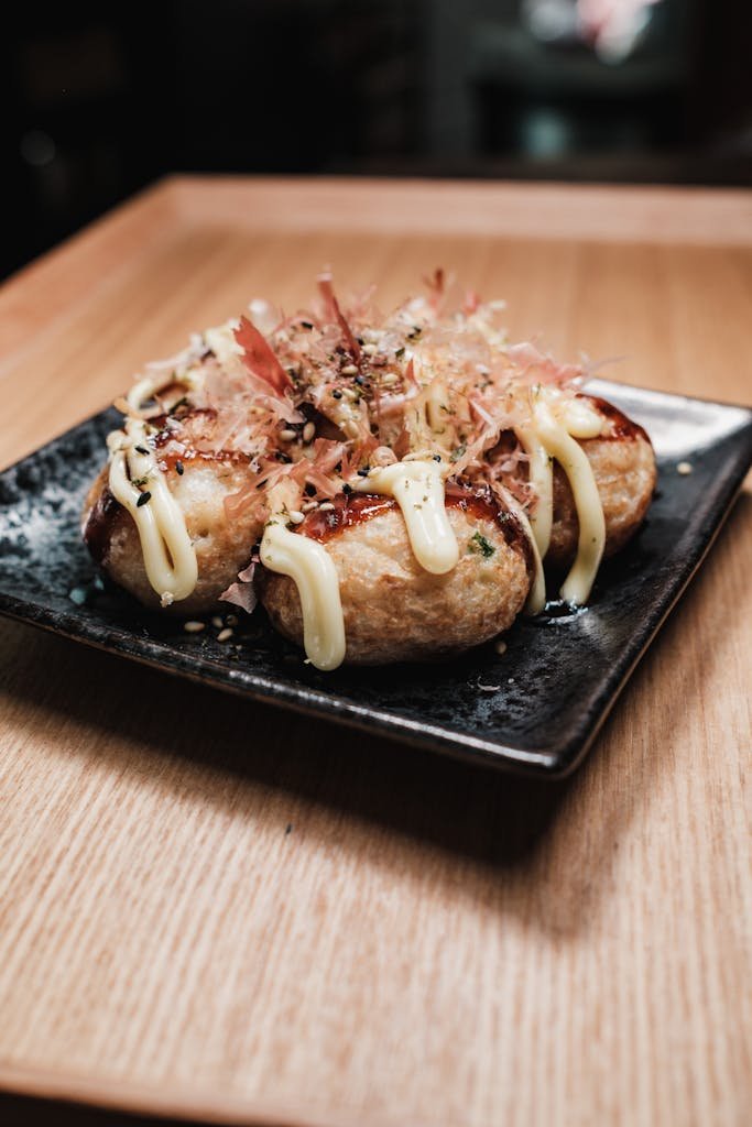 Close-up of Japanese Takoyaki topped with bonito flakes and mayo on a black plate.