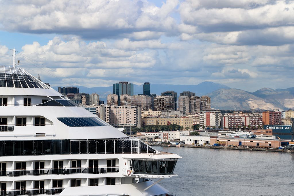 Is Naples Worth Visiting? 15 Pros and 5 Cons 6 Cruise liner docked at Napoli port with scenic cityscape and cloudy sky backdrop.