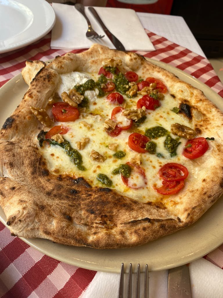 Delicious Neapolitan pizza topped with cherry tomatoes, pesto, and walnuts on a rustic plate.