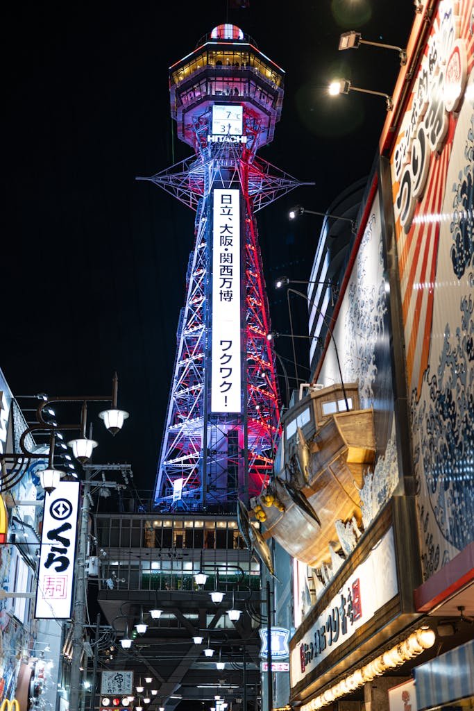 Dynamic night view of Osaka's illuminated Tsutenkaku Tower surrounded by city lights and vibrant signage.