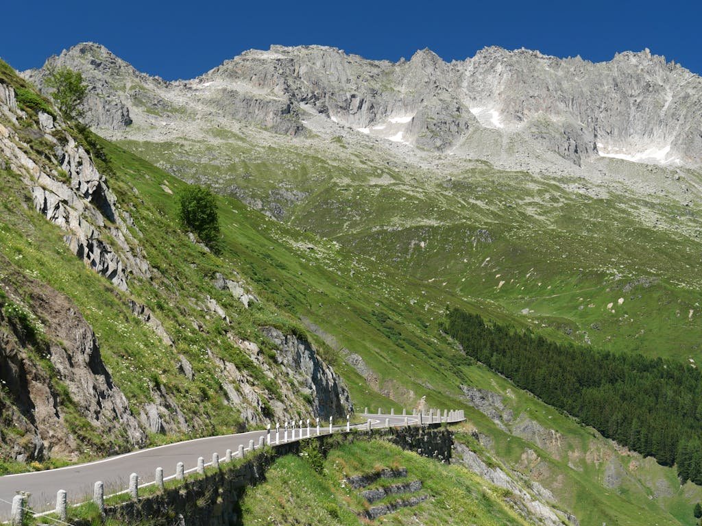Explore the winding Furka Pass road offering stunning views of Swiss Alps and green landscapes.