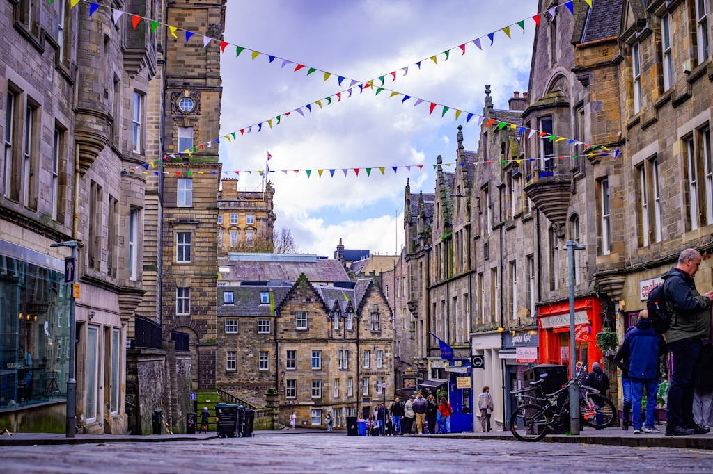 Lively Edinburgh street lined with historic architecture and festive bunting above. Perfect depiction of Scottish urban charm.