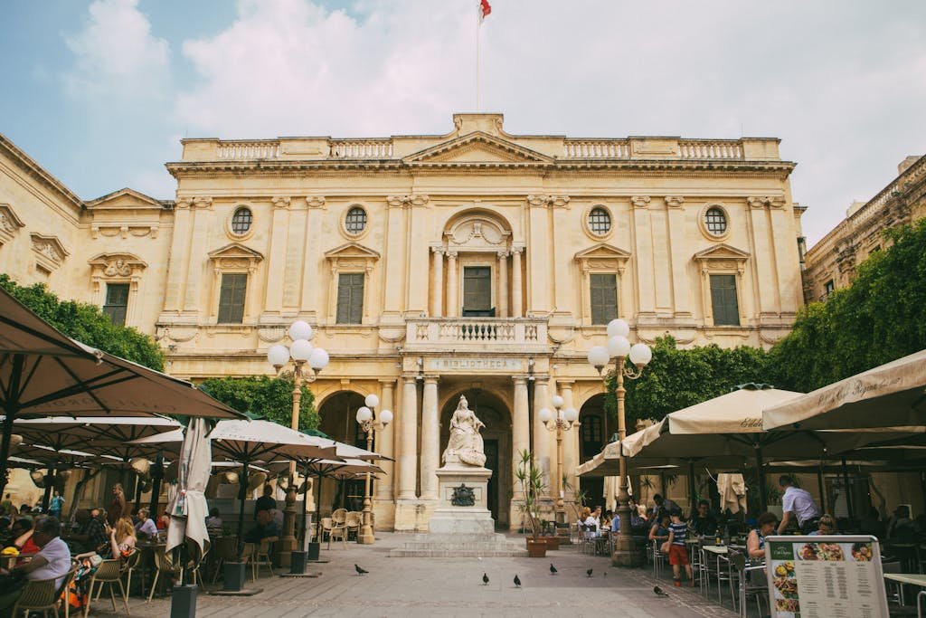 Outdoor café with people near the National Library of Malta in Valletta, featuring elegant courtyard architecture.