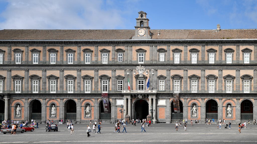 People strolling in Piazza del Plebiscito with the Royal Palace facade in Naples, Italy.