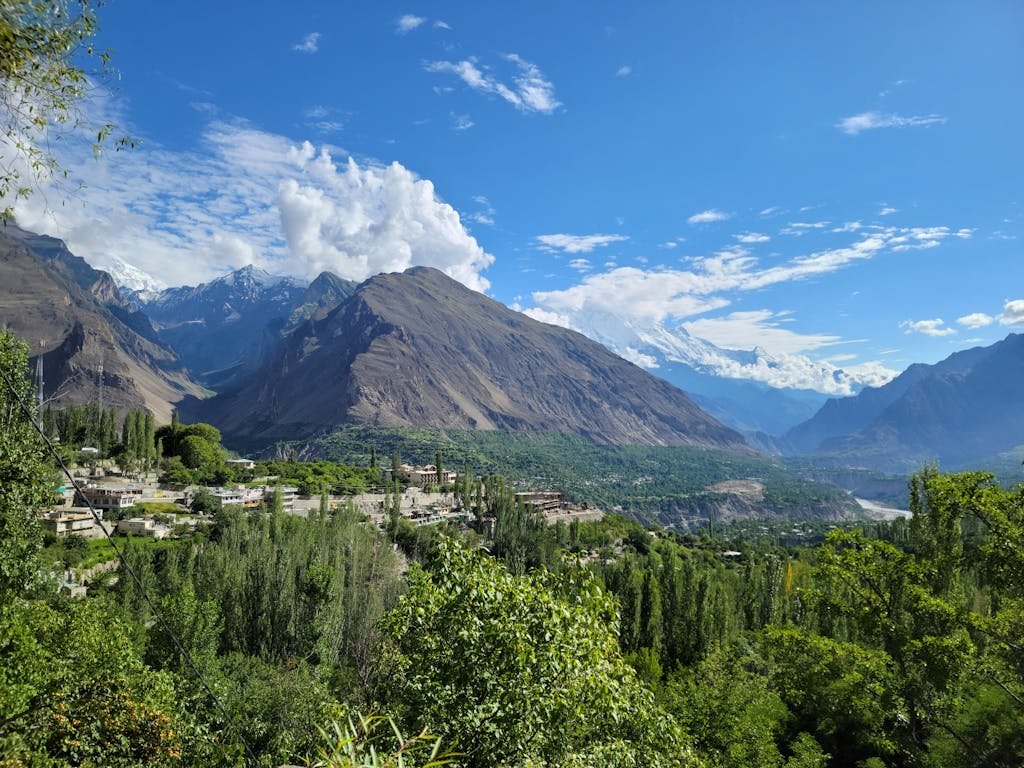 Scenic summer travel view of Hunza Valley with lush greenery and majestic mountains under a clear blue sky.