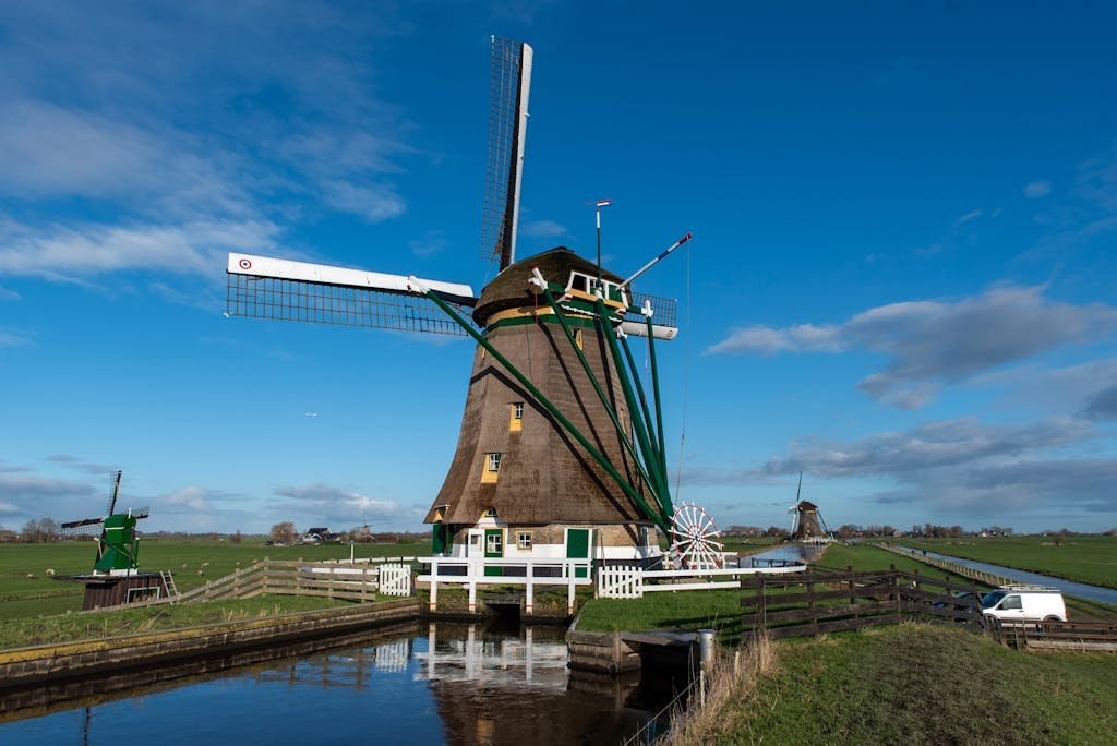 Scenic view of a classic Dutch windmill by a canal on a bright day with clear skies.