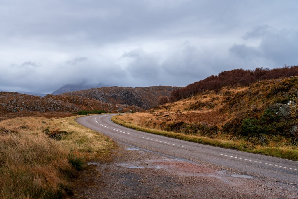 Scenic view of a winding road through the autumn-colored Scottish Highlands under a cloudy sky.