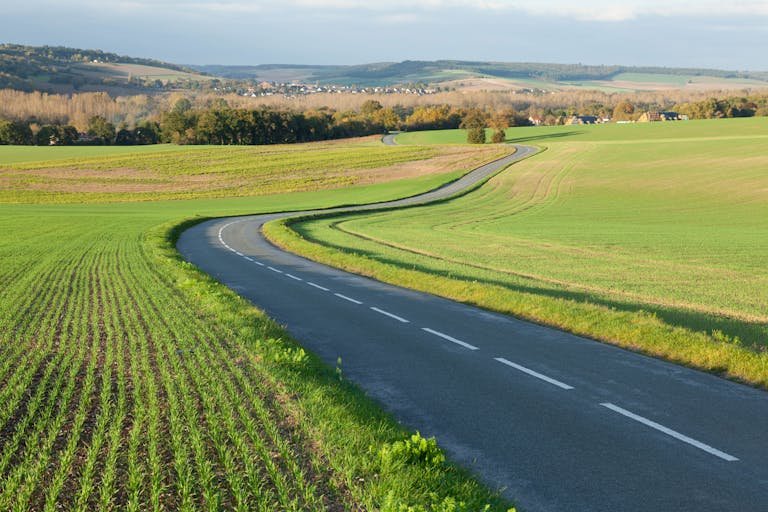 Serene countryside road through green fields in Gommecourt, IDF, France.