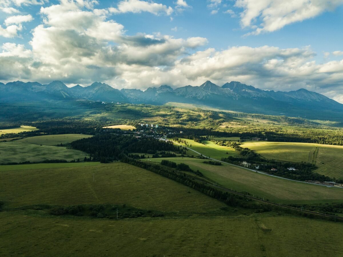 Stunning aerial view of Vysoké Tatry in Slovakia, showcasing lush fields and dramatic mountain ranges.