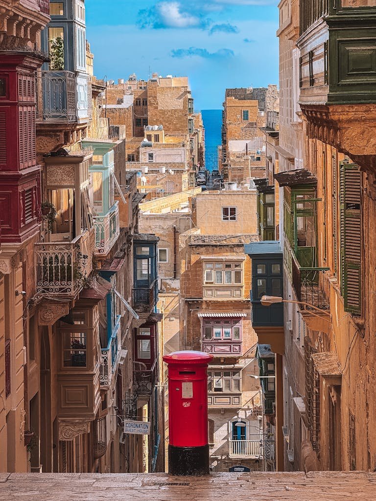 Vibrant traditional balconies line the historic streets of Valletta, Malta, leading to the sea.
