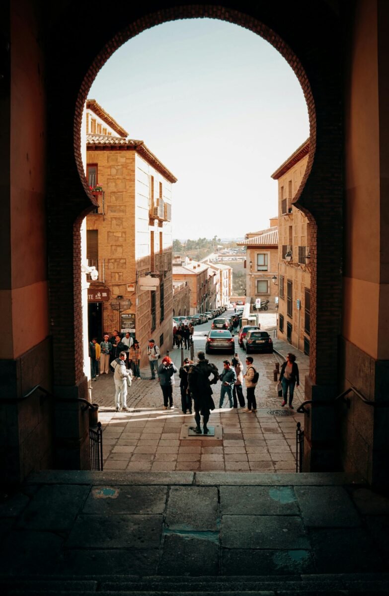 Home 19 View through a medieval archway onto a bustling Spanish street in Toledo, Spain.