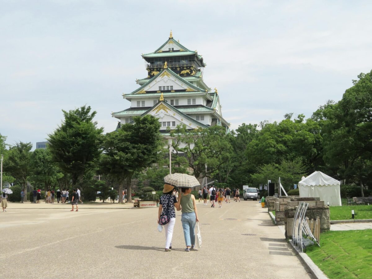 Visitors with umbrellas walking towards Osaka Castle, Osaka, Japan, on a bright summer day.