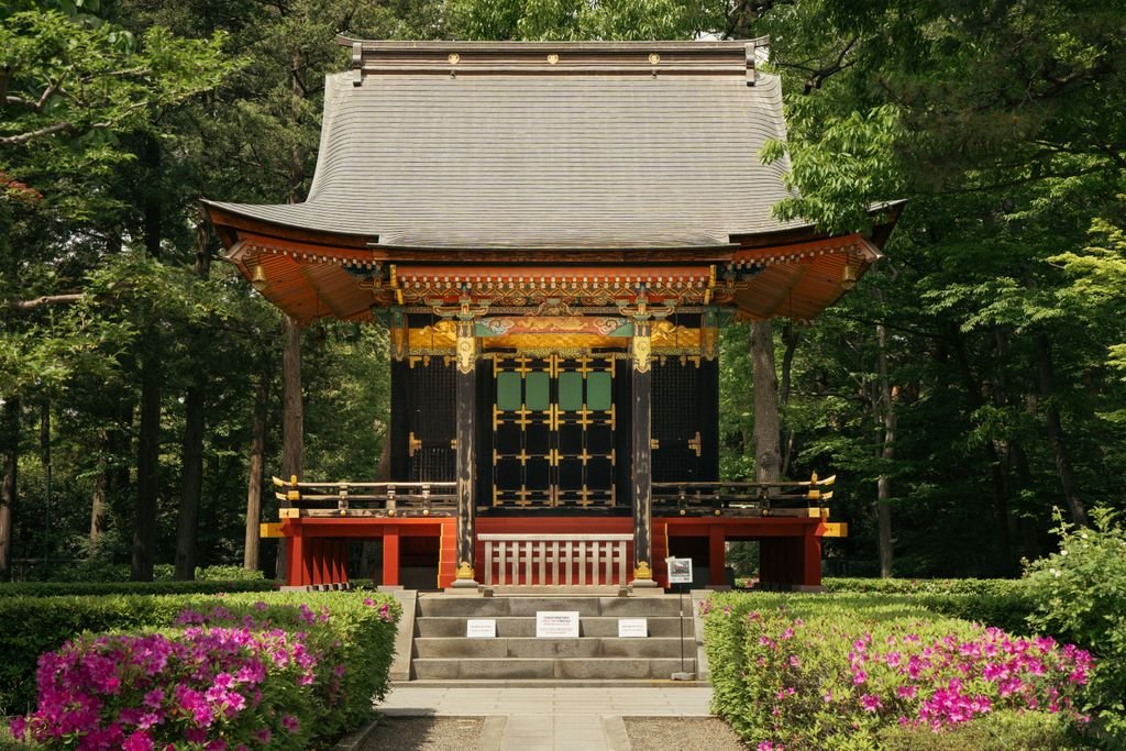 A beautiful traditional Japanese temple surrounded by lush greenery and pink azaleas in a serene Tokyo garden.