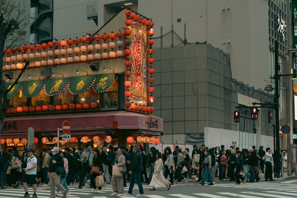 A lively street in Tokyo's Shinjuku with illuminated signs and crowds crossing.