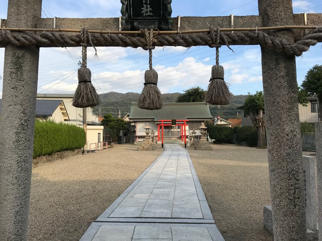A serene view of a traditional Japanese Shinto shrine with a prominent torii gate under a blue sky.