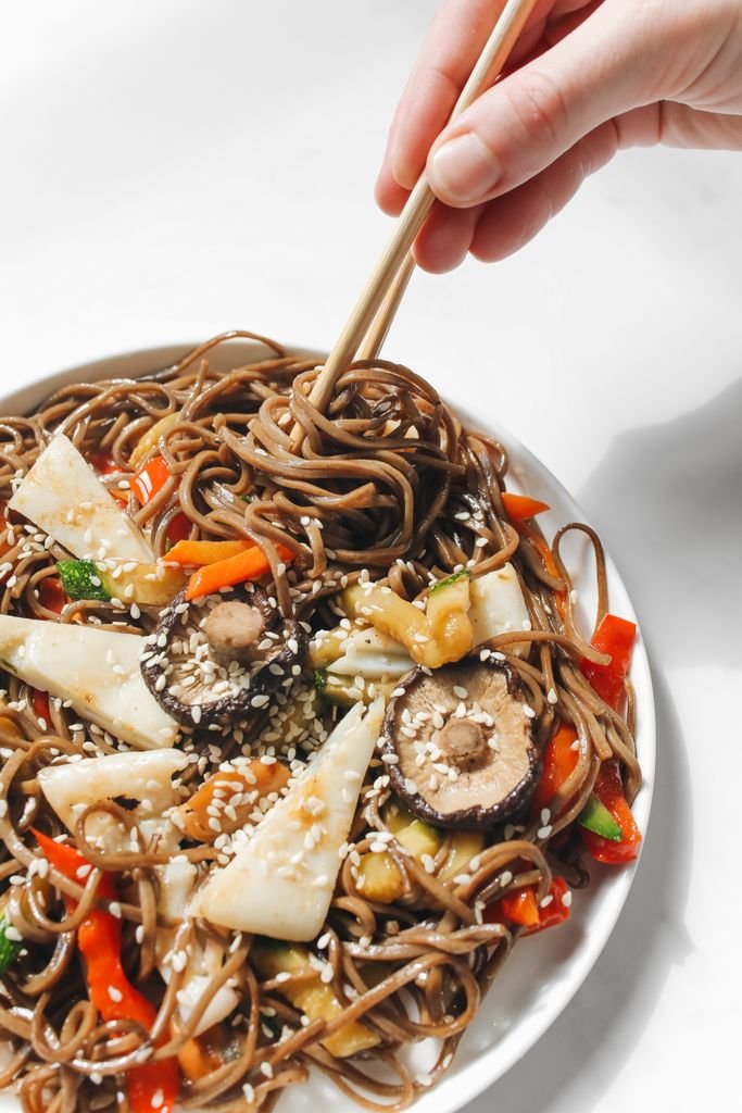 Close-up of soba noodles with mushrooms and vegetables, garnished with sesame seeds.