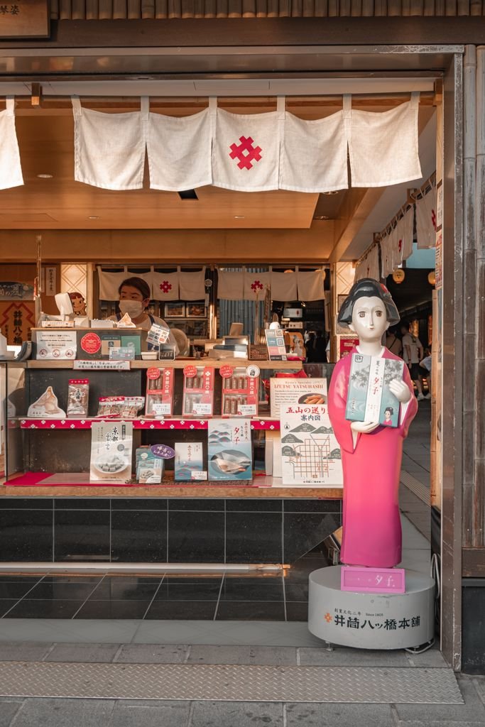 Arashiyama Bamboo Forest Kyoto: Is It Worth Visiting? 10 Exterior of a Japanese shop in Kyoto featuring a traditional figure statue and various items for sale.