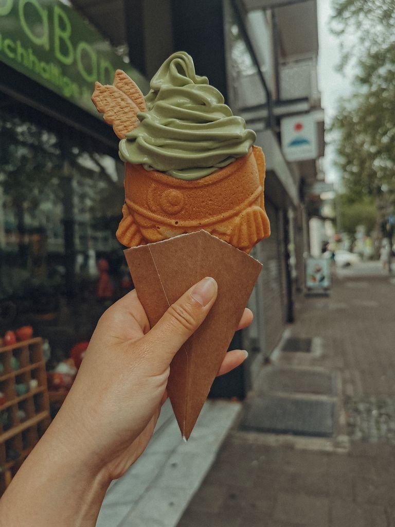 Nara Day Trip Guide: 10 Best Things to Do in Nara 9 Hand holds matcha ice cream in fish-shaped cone on urban street.