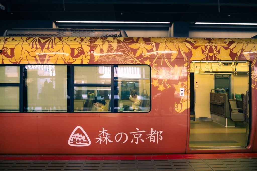 Kyoto metro train in vibrant red livery featuring botanical patterns at station.