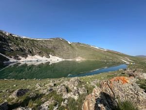 Dudipatsar Lake Trek: Pakistan's Most Beautiful Alpine Lake 2 Peaceful mountain lake reflecting rocky slopes and patches of snow under clear blue sky.