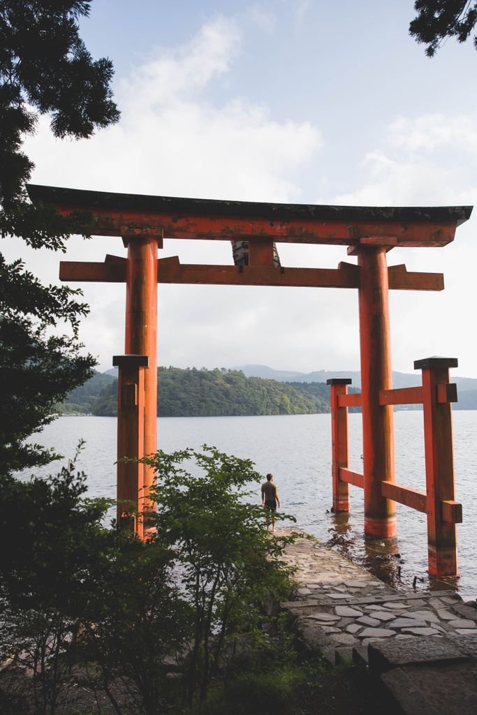 Red torii gate overlooking a serene lake in Hakone, Japan, surrounded by lush greenery.