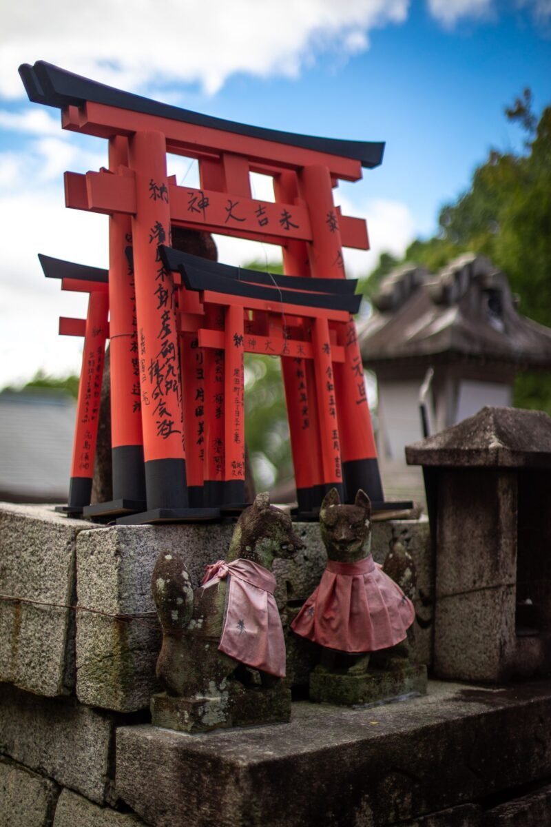 Traditional Japanese shrine view with red torii gates and fox statues in Kyoto, Japan.