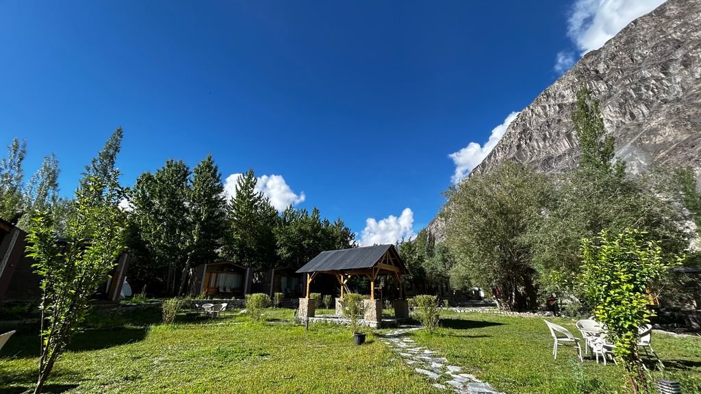 15 The Best Things to Do in Skardu for an Unforgettable Trip 14 A picturesque gazebo amidst lush greenery with a mountain backdrop on a sunny day in northern Pakistan.