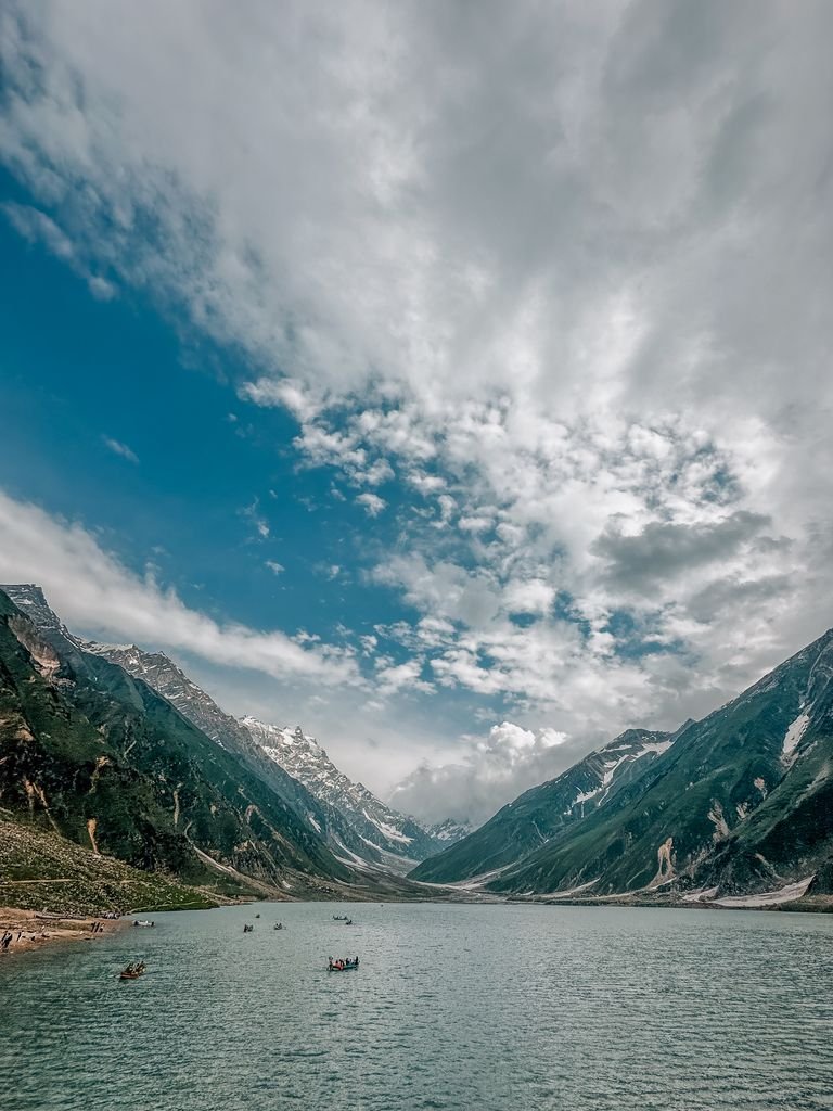 A serene mountain lake set between snow-capped peaks under a dramatic sky, perfect for adventure travelers.