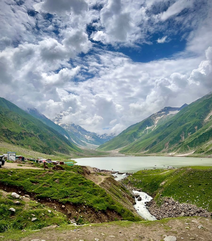 Beautiful landscape of a lake surrounded by lush green mountains and a vibrant blue sky in Naran, Pakistan.