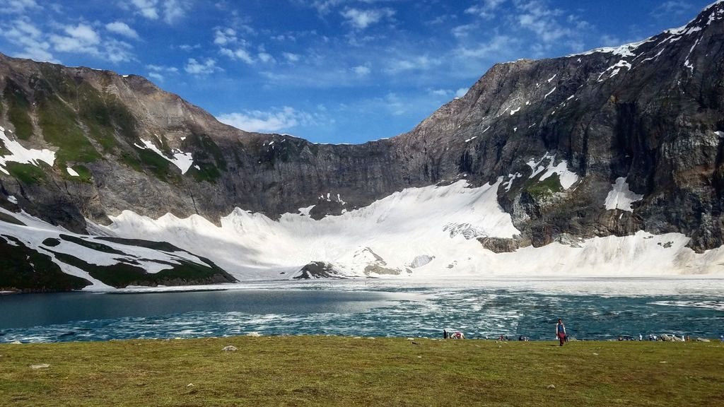 15 The Best Things to Do in Skardu for an Unforgettable Trip 5 Breathtaking mountain landscape featuring a glacial lake, grassy meadow, and snow-covered peaks under a clear blue sky.