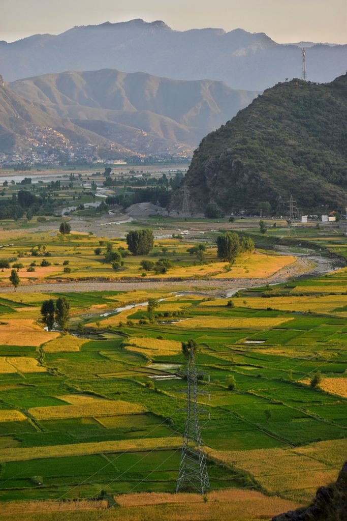 Expansive aerial landscape of agricultural fields in Kabal, Swat Valley Khyber Pakhtunkhwa, Pakistan with mountains in the backdrop.