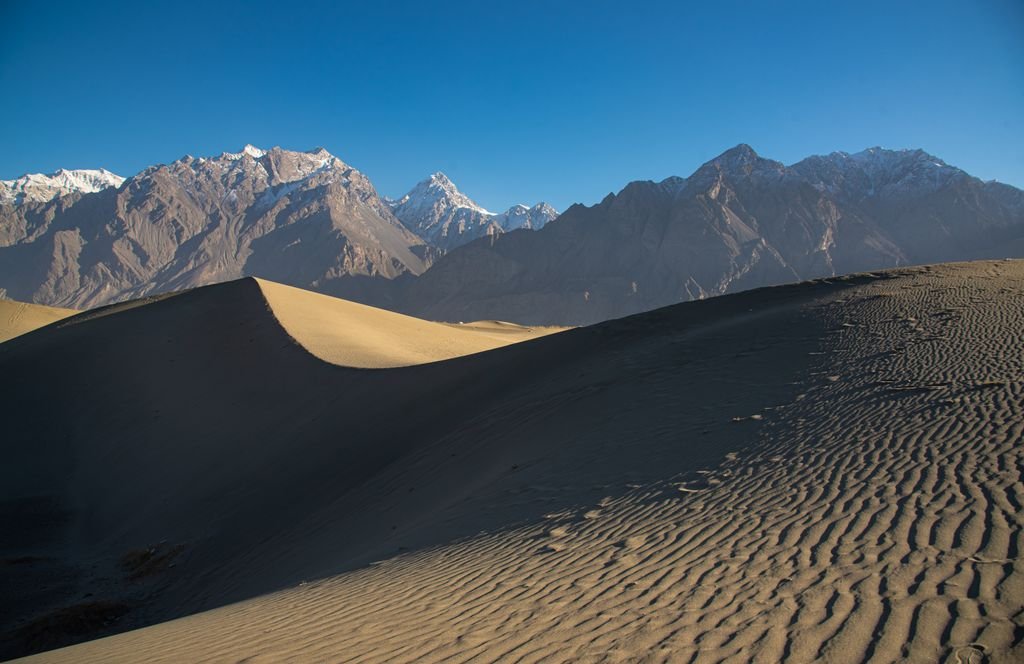 15 The Best Things to Do in Skardu for an Unforgettable Trip 7 Stunning dune landscape against snow-capped mountains in Skardu, offering a breathtaking natural vista.