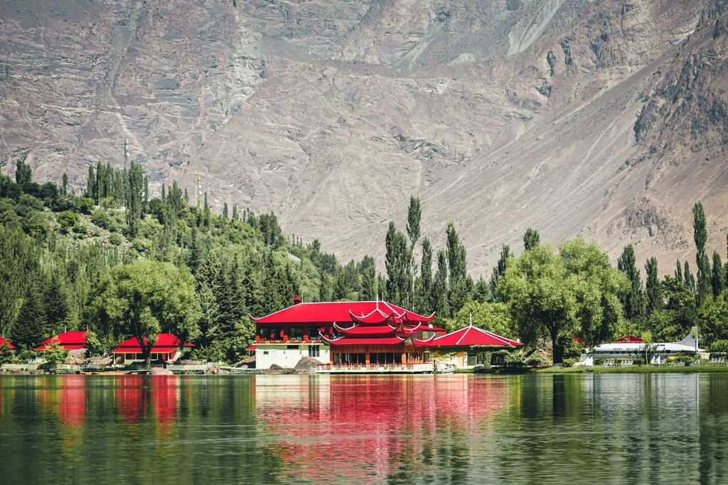 15 The Best Things to Do in Skardu for an Unforgettable Trip 4 Stunning lake view with traditional architecture and vibrant red roofs framed by mountains and trees.