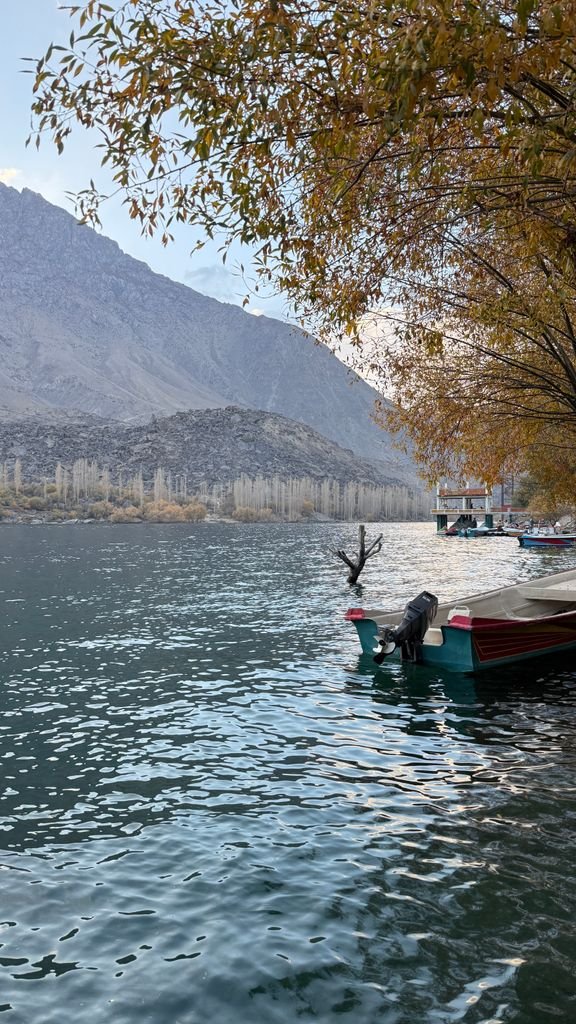 15 The Best Things to Do in Skardu for an Unforgettable Trip 10 Tranquil view of boats on a serene Skardu lake surrounded by mountains and autumn trees.
